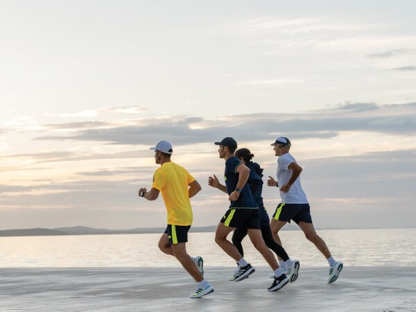 Keturi bėgimo dalyviai bėga paplūdimiu.